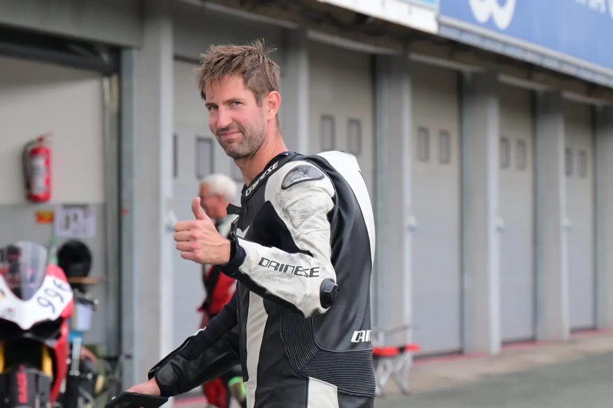 Racer in leathers giving a thumbs up in the paddock after a session